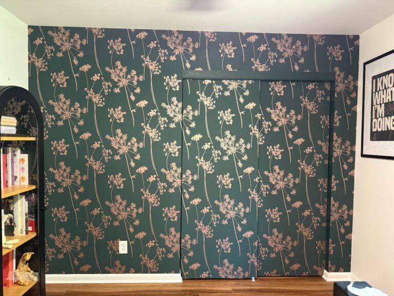 Dark green wallpaper with a blush Queen Anne’s lace pattern on an accent wall and closet doors